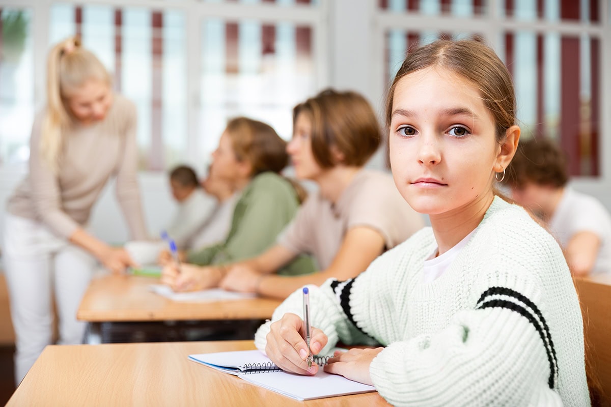 Young,Girl,Sitting,At,Desk,In,Classroom,And,Looking,At